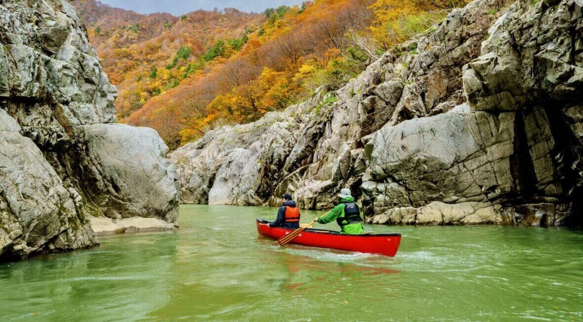 赤く色づいた山の紅葉の景色を楽しみながらカヌーで川下り