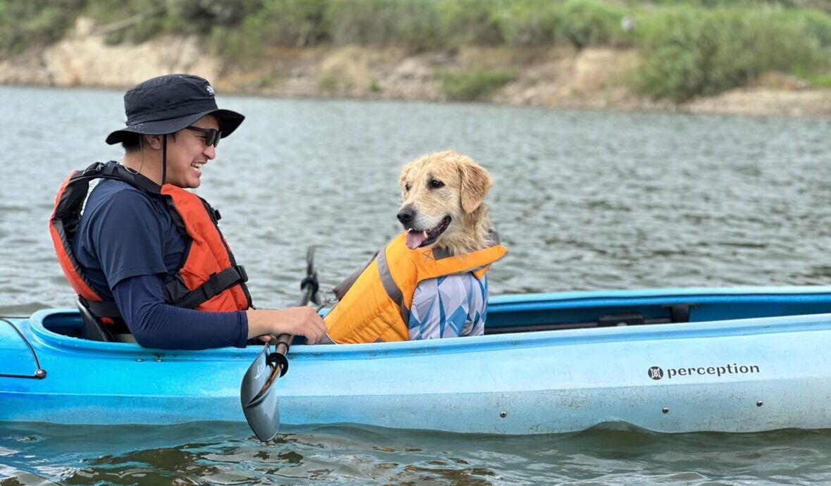 愛犬と一緒にカヌーに乗り川を泳ぐ男性