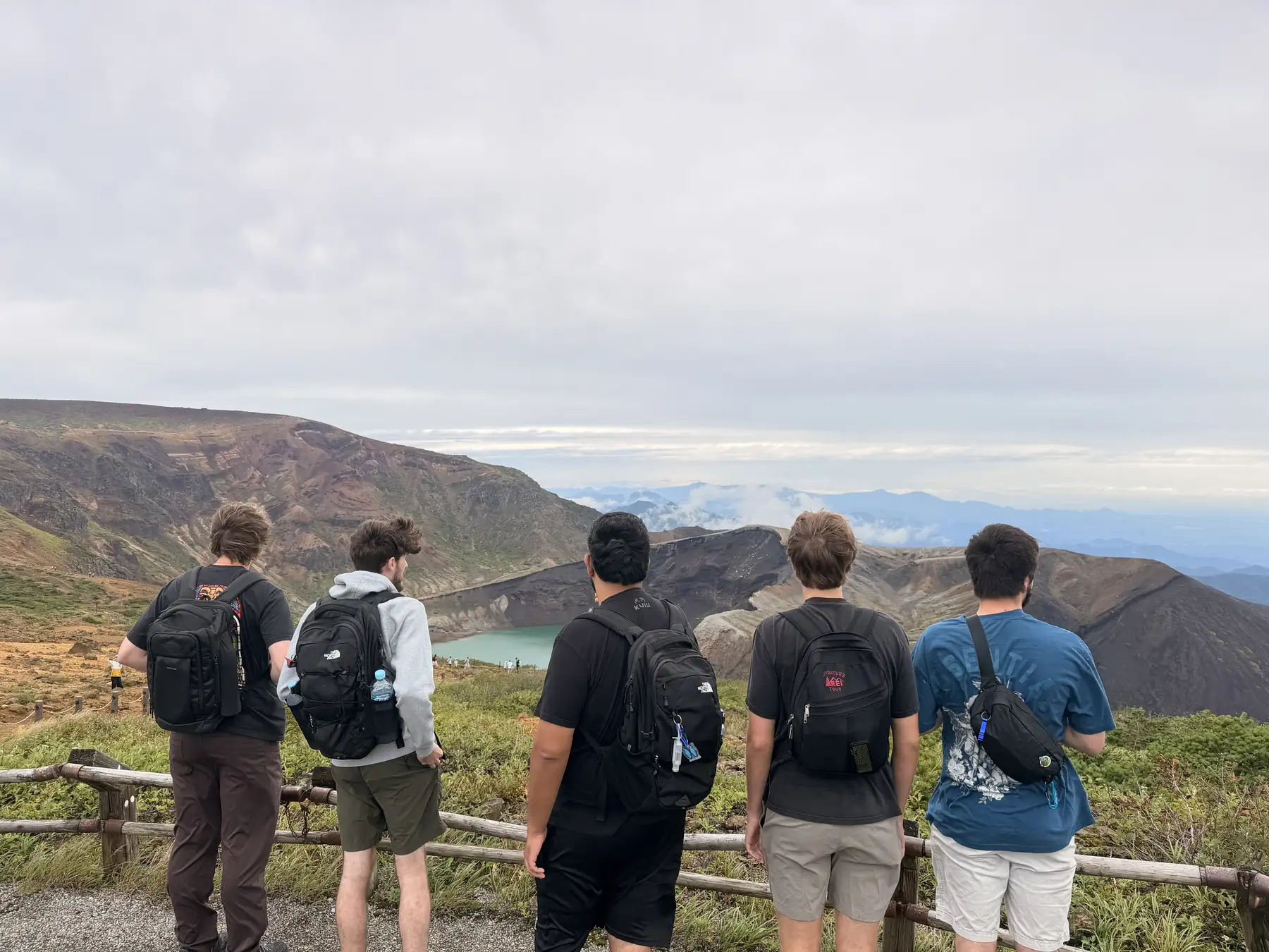 Five travelers on the rim of Mount Zao look down on the emerald Okama crater lake
