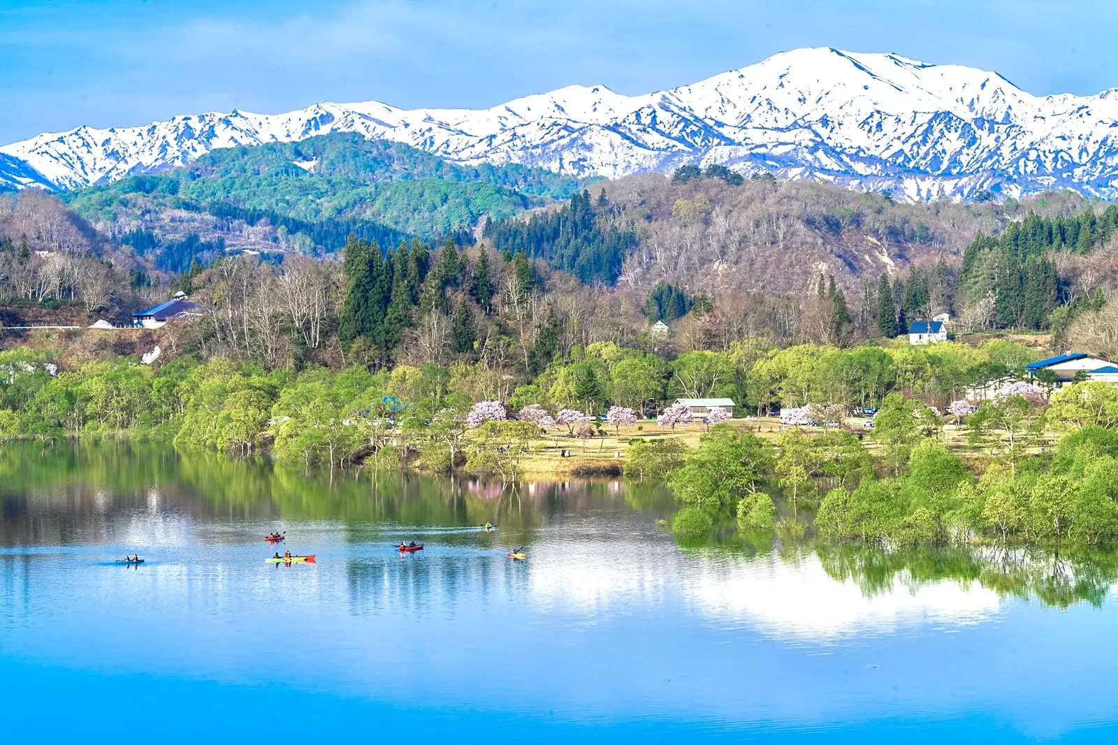 Lake Shirakawa in spring, with the snow-covered Iide mountains behind and canoes on the water