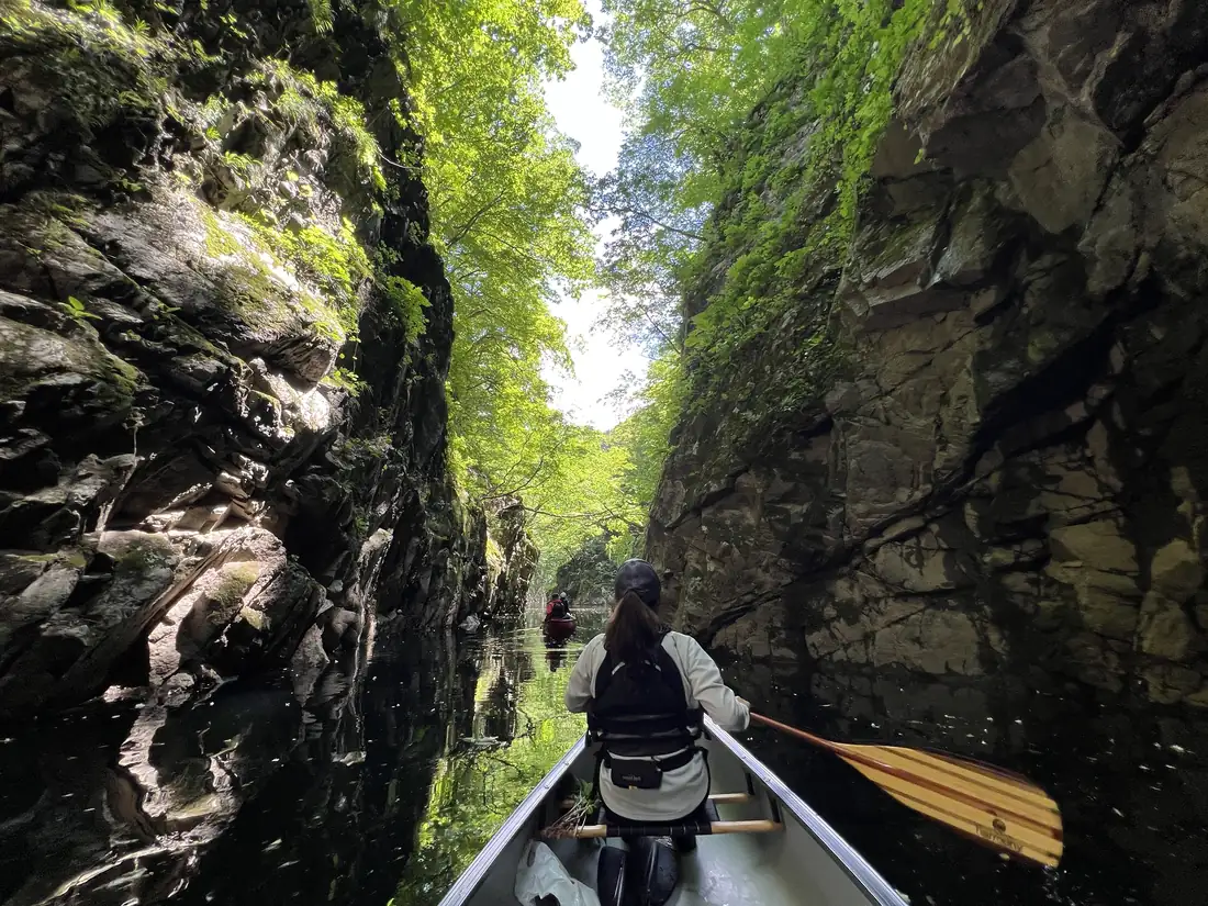 A paddler seen from behind, entering a narrow gorge between rock walls