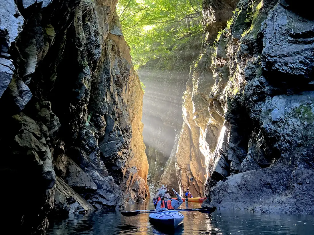 Shafts of light fall between the sheer granite walls of Mifuchi Gorge, with small kayaks on the lake below
