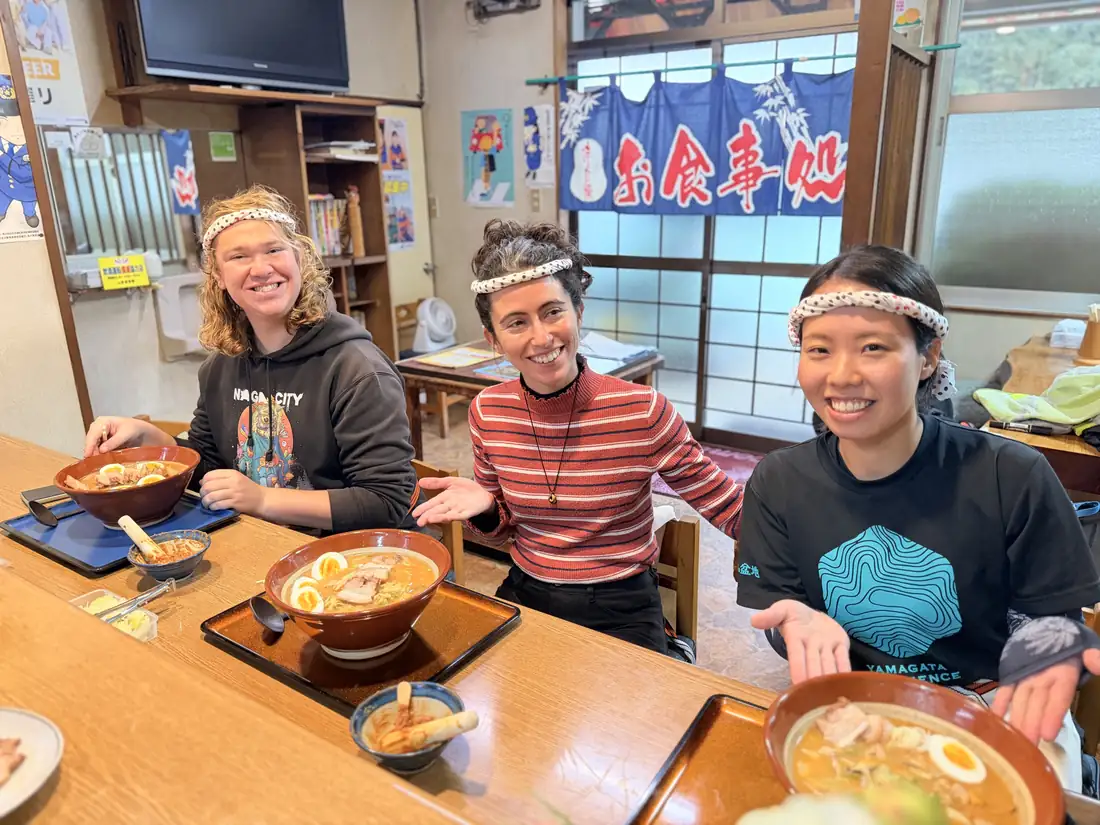Three people smile behind bowls of ramen they have just made