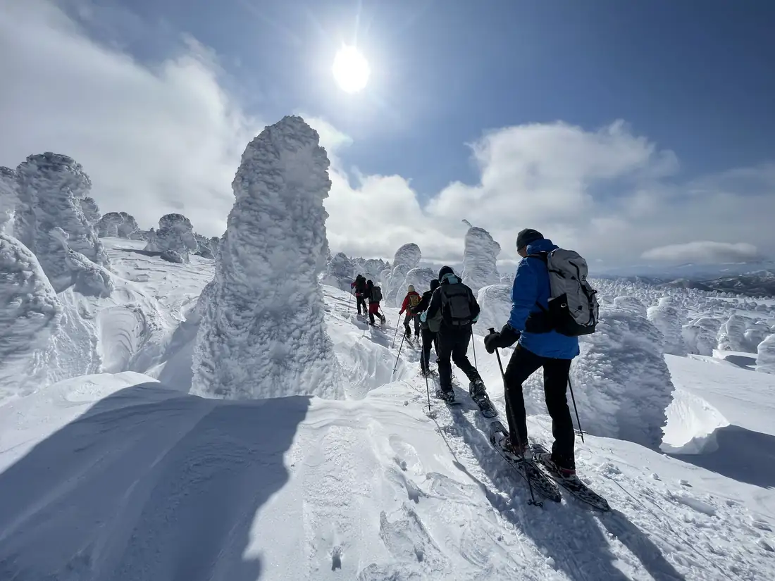 Snowshoers walk in single file past a towering snow monster